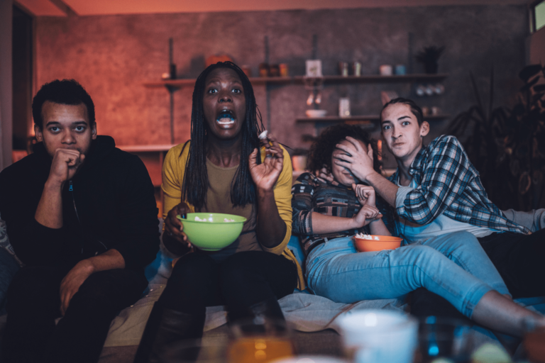 four people sitting on a couch watching a thrilling movie