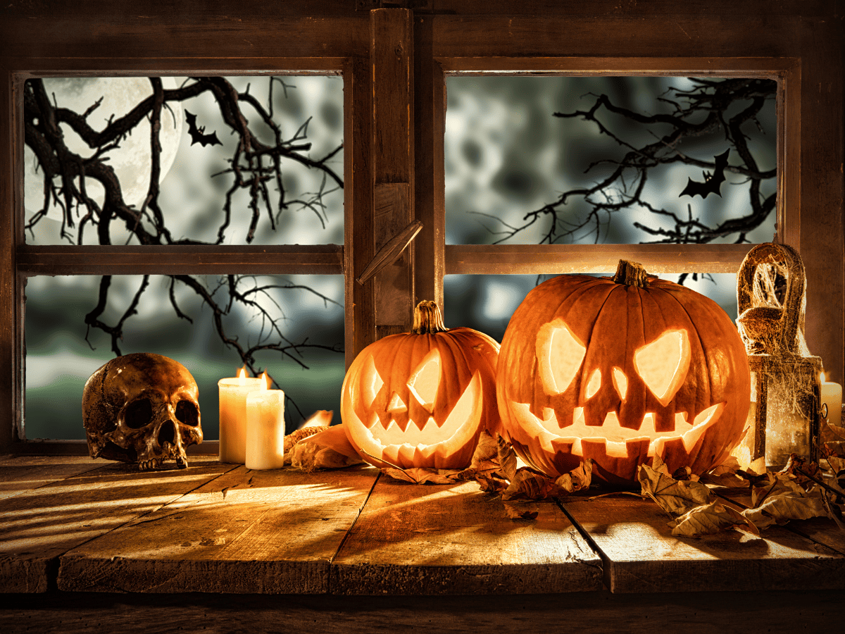 two lit jack o'lanterns on a table in front of a window with two lit candles and a skull